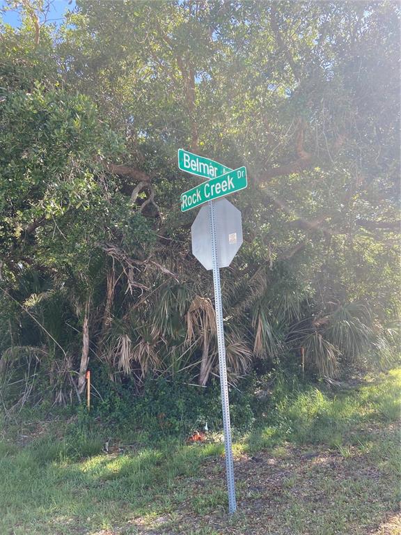 A street sign for Belmar and Rock Creek Drive stands in front of dense trees — 1189 BELMAR AVE, PORT CHARLOTTE, FL