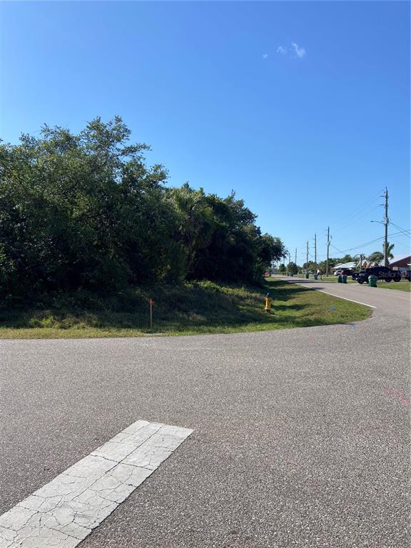 A vacant, tree-lined corner lot sits next to a paved road with a fire hydrant — 1189 BELMAR AVE, PORT CHARLOTTE, FL