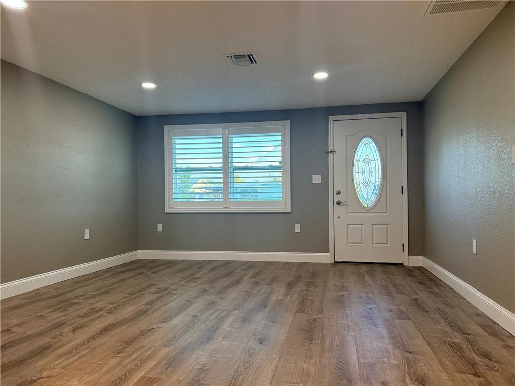 A room with gray walls, wood-look flooring, a white front door, and plantation shutters — 6623 BOATYARD DRIVE, HUDSON, FL
