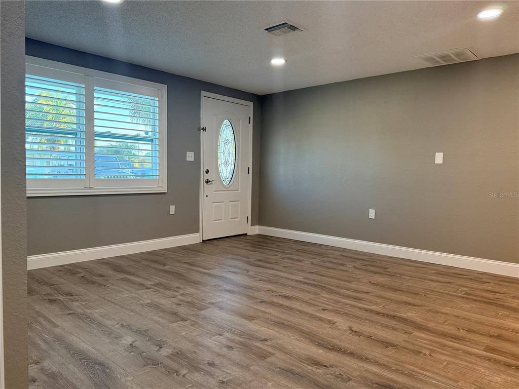 An empty room with gray walls, wood-look flooring, a front door, and plantation shutters — 6623 BOATYARD DRIVE, HUDSON, FL