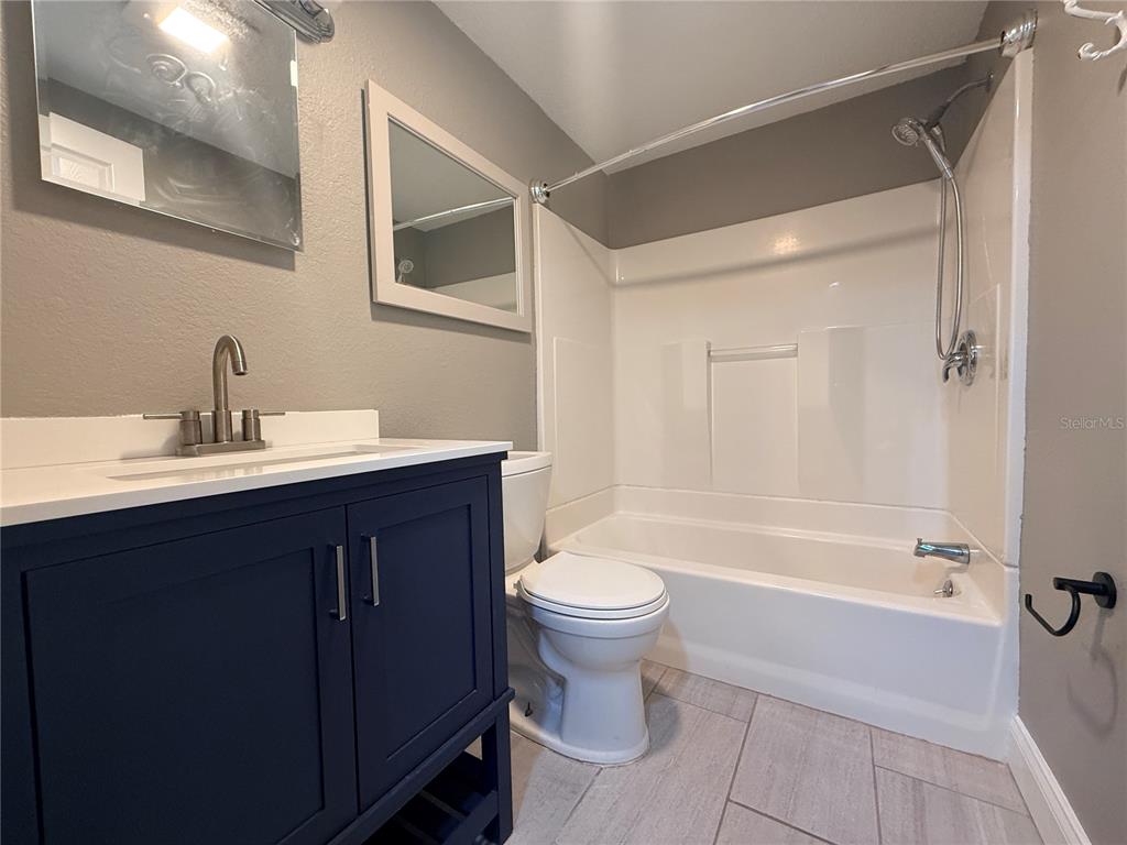 A bathroom features a dark blue vanity, a white toilet, and a shower-tub combination — 6623 BOATYARD DRIVE, HUDSON, FL