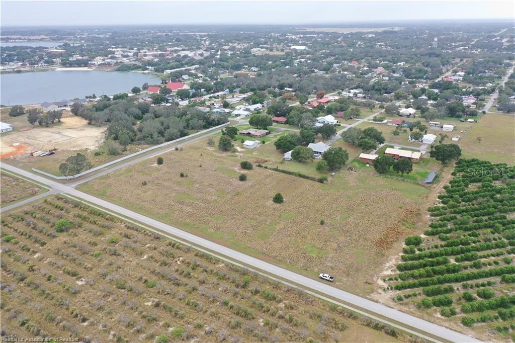 An aerial view shows a large, vacant grassy lot bordered by roads and nearby houses — 525 E WINTHROP STREET, AVON PARK, FL