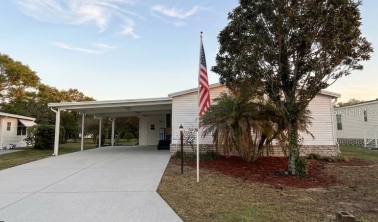 A white manufactured home features a large concrete carport and an American flag in front — 5320 LAUREL OAK DRIVE, WINTER HAVEN, FL