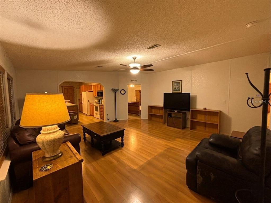A living room with wood-look flooring, a ceiling fan, and an open view into the kitchen — 5320 LAUREL OAK DRIVE, WINTER HAVEN, FL