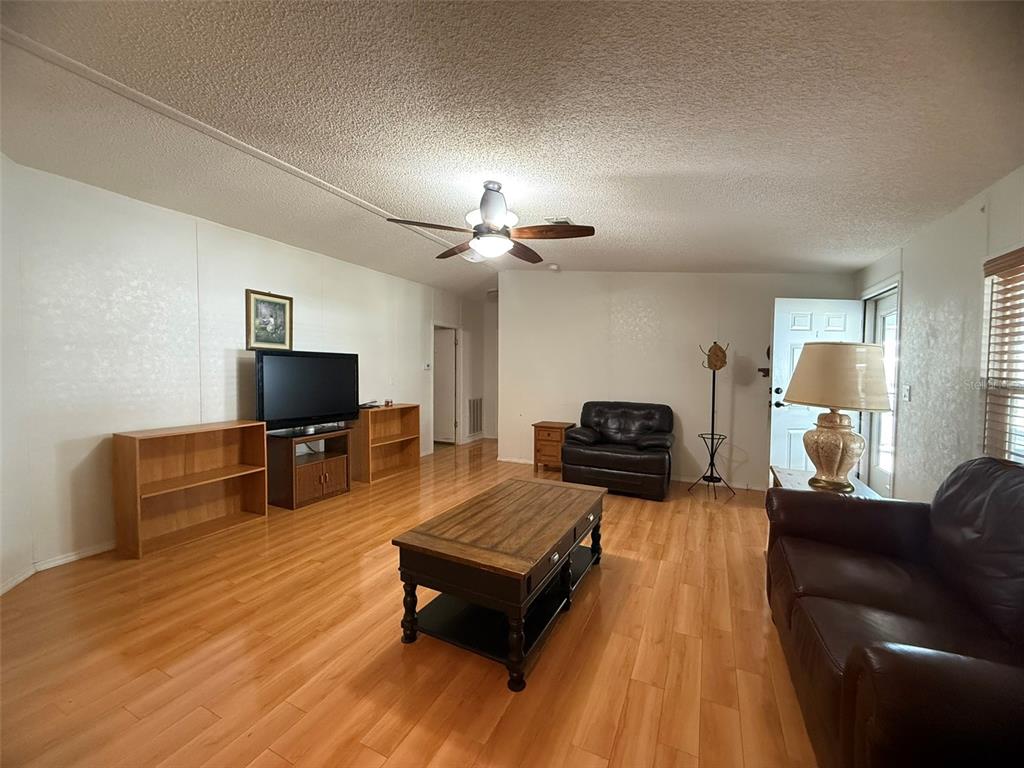 A living room features light wood-look flooring, a ceiling fan, and dark leather furniture — 5320 LAUREL OAK DRIVE, WINTER HAVEN, FL