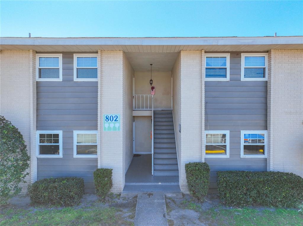 A two-story apartment building exterior features brick walls, gray siding, and a central staircase — 802 SKY LAKE CIRCLE UNIT C, ORLANDO, FL