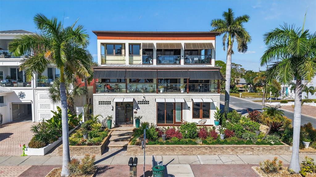 A three-story house with balconies, large windows, and a landscaped front yard with palm trees — 5659 SHORE BOULEVARD S, GULFPORT, FL