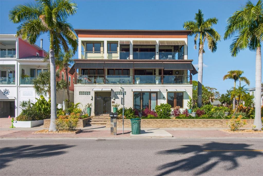 A three-story coastal home features balconies, large windows, and palm trees in the front yard — 5659 SHORE BOULEVARD S, GULFPORT, FL