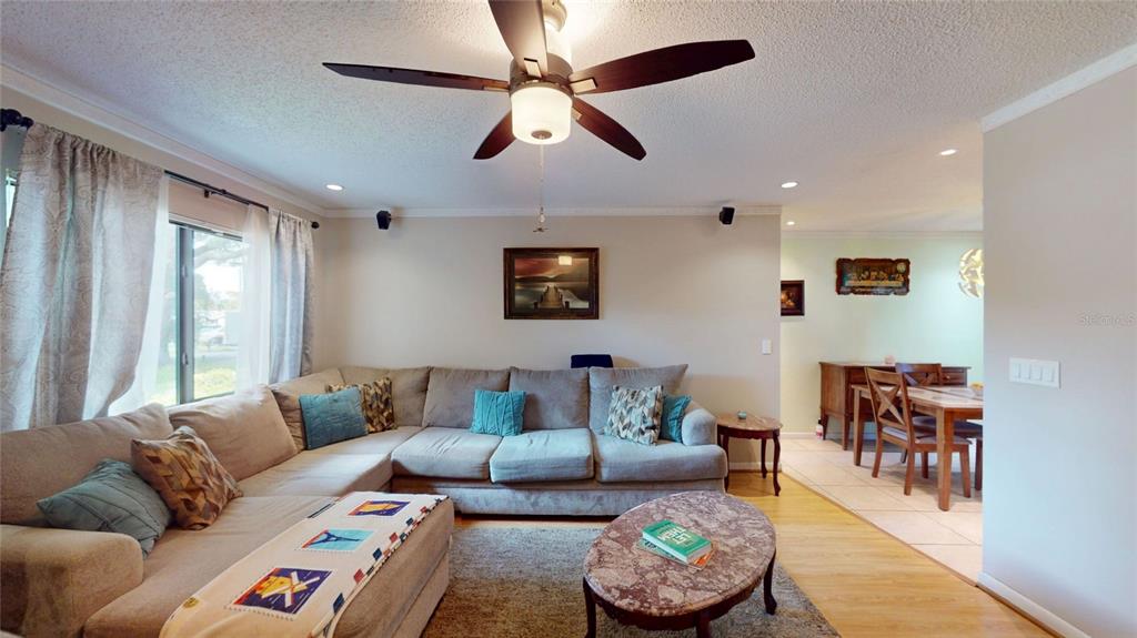 A living room features a large sectional sofa, a ceiling fan, and a marble coffee table — 6960 PINECREST LANE N, PINELLAS PARK, FL