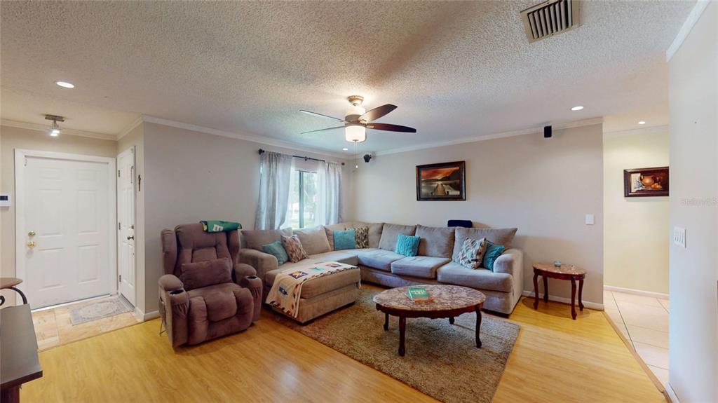 A living room features a sectional sofa, a recliner, a coffee table, and wood flooring — 6960 PINECREST LANE N, PINELLAS PARK, FL