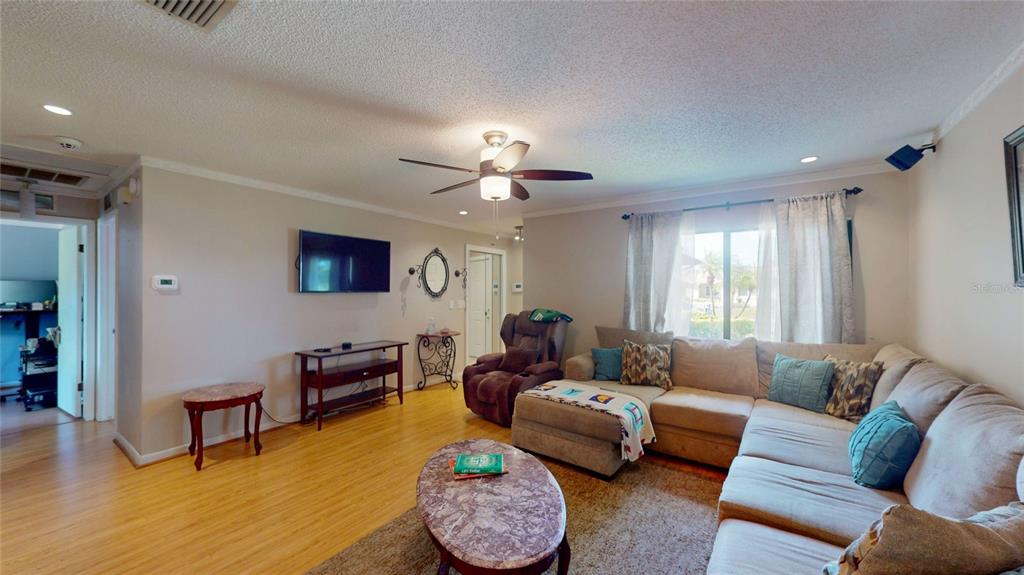 A living room features a sectional sofa, a ceiling fan, and light-colored wood flooring — 6960 PINECREST LANE N, PINELLAS PARK, FL