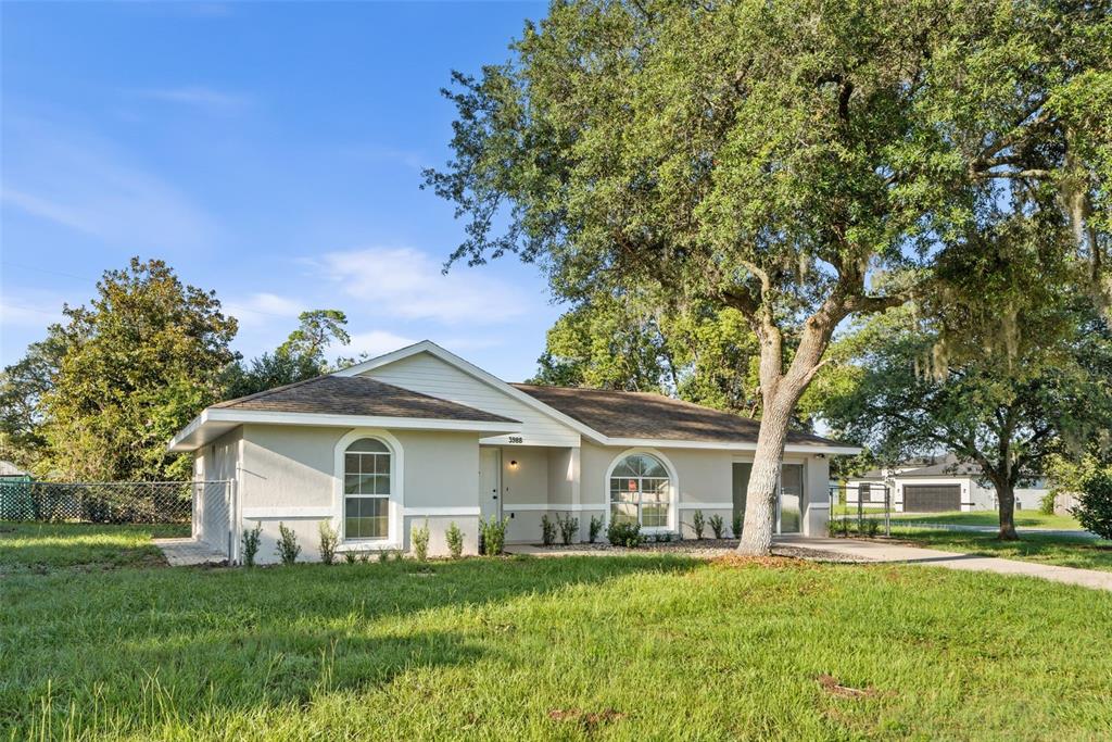A single-story house with a light-colored exterior, arched windows, and a large tree in front — 3988 SW 169TH LN, OCALA, FL
