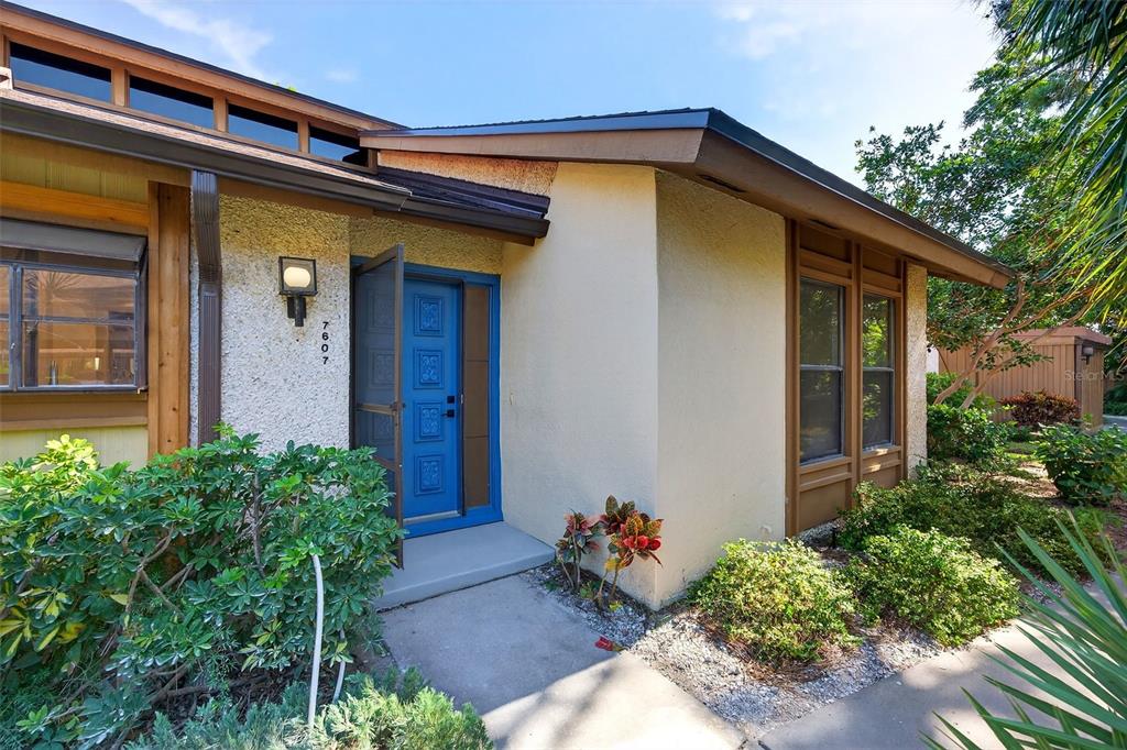 The exterior of a house features a blue front door, stucco walls, and brown trim — 7607 4TH AVENUE W, BRADENTON, FL