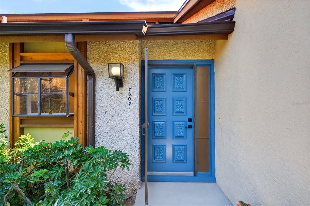 A bright blue front door with square panels sits next to a vertical glass sidelight — 7607 4TH AVENUE W, BRADENTON, FL