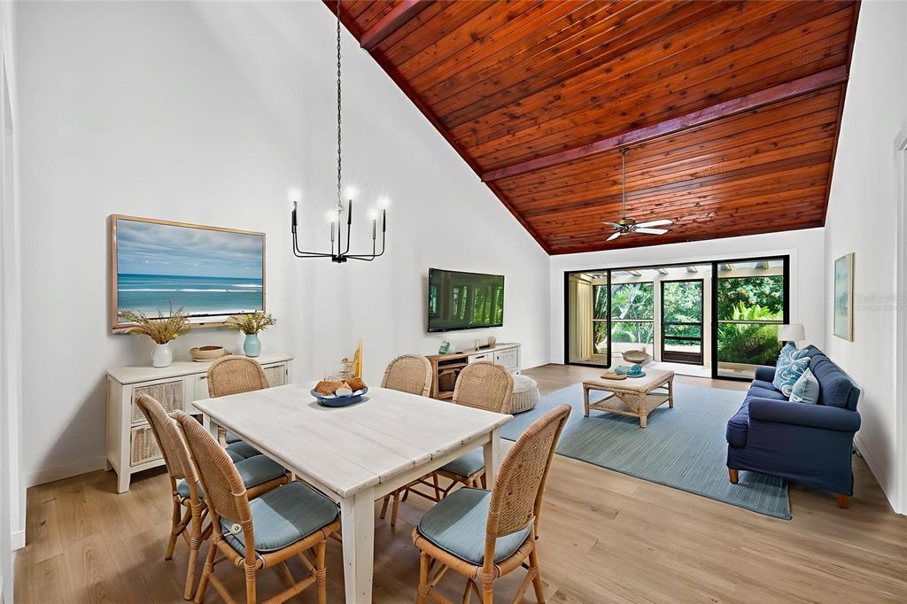 A dining and living area features a vaulted wood-plank ceiling and sliding glass doors — 7607 4TH AVENUE W, BRADENTON, FL
