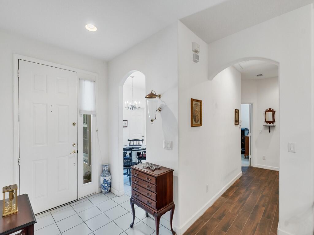 An entryway features a white front door, tiled flooring, a wooden chest, and arched doorways — 3830 Nags Head Place SW, Vero Beach FL 32968, VERO BEACH, FL