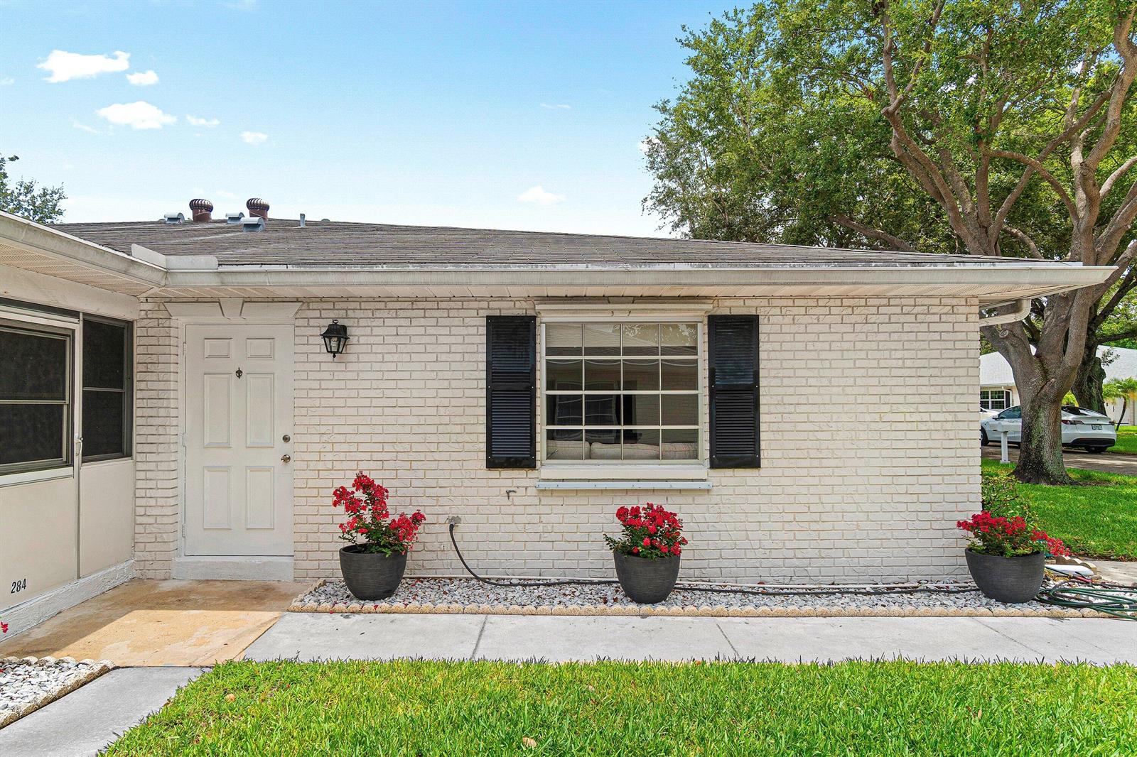 A single-story brick house exterior features a white front door, black shutters, and potted flowers — 10098 S 40th Drive S, Boynton Beach FL 33436, BOYNTON BEACH, FL