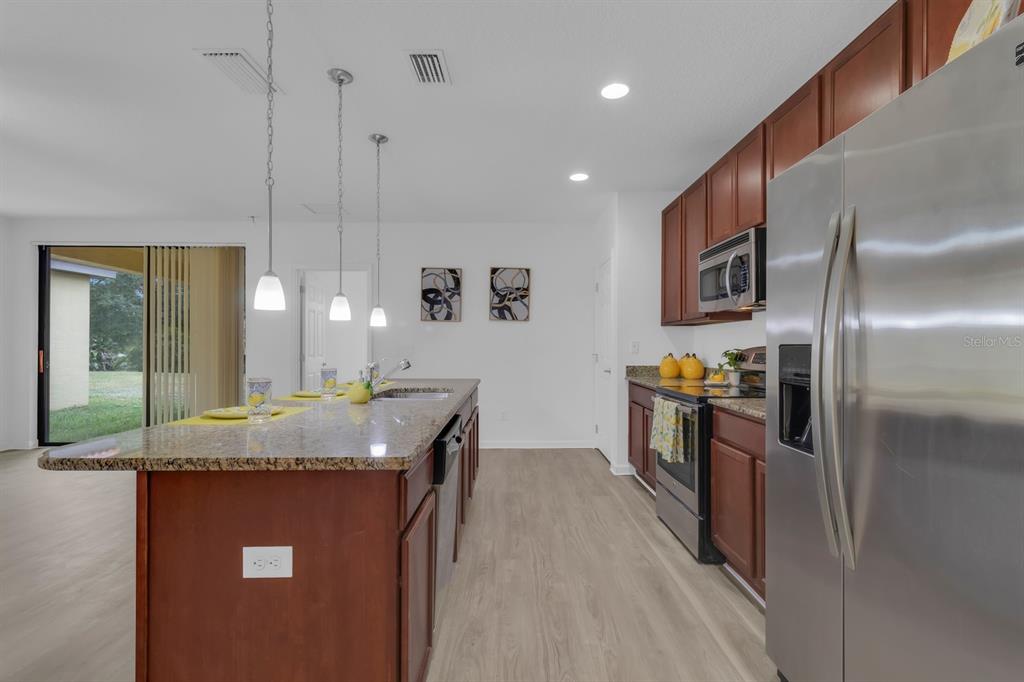 A kitchen features dark wood cabinets, granite countertops, stainless steel appliances, and a center island — 2943 CASABELLA DRIVE, KISSIMMEE, FL