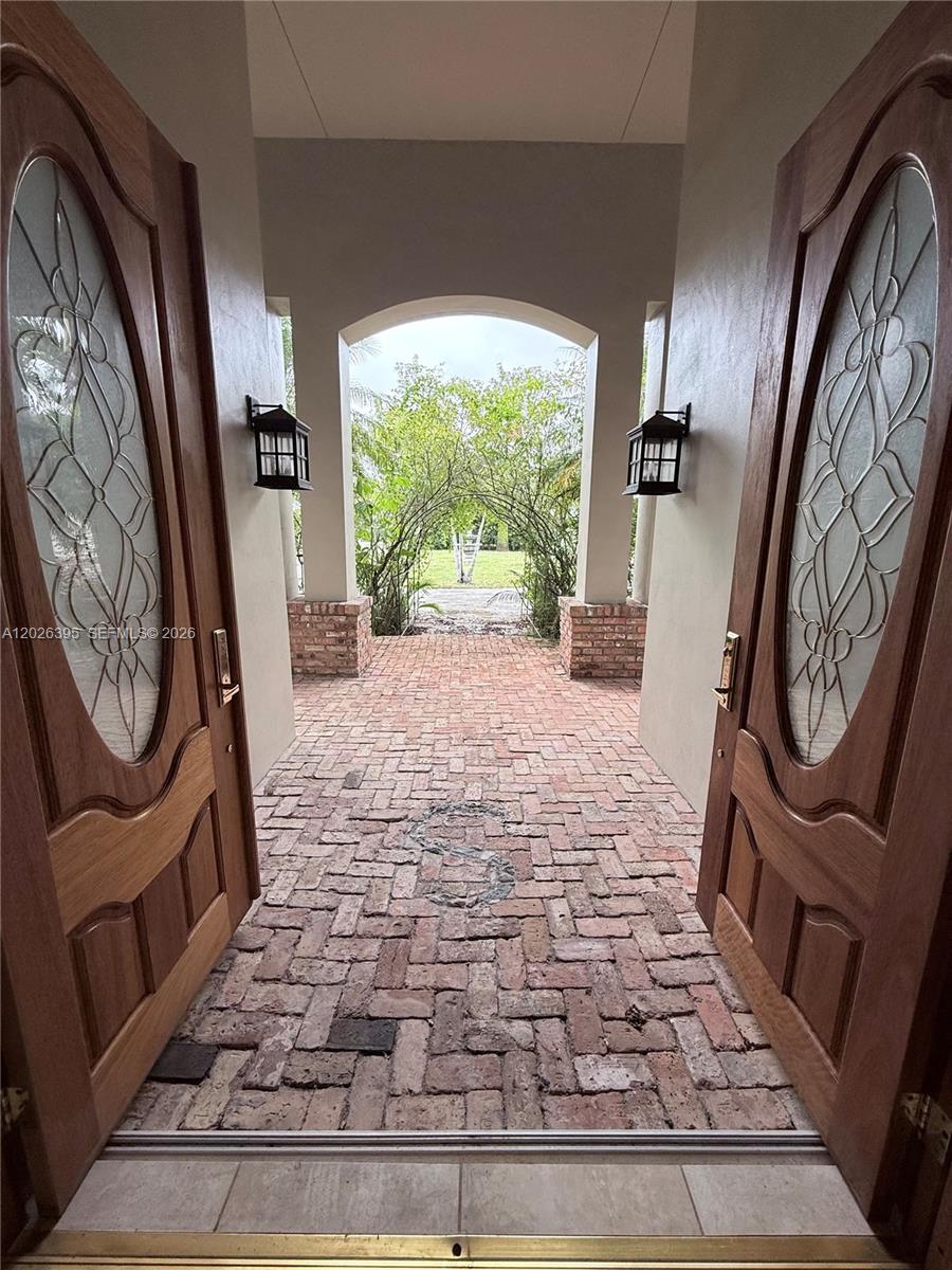 An open double door reveals a brick-paved entryway leading to an outdoor garden archway — HOMESTEAD, FL
