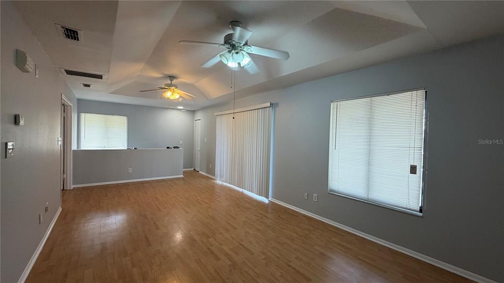 An empty living room features light wood flooring, gray walls, ceiling fans, and sliding doors — 4323 PINEBARK AVENUE UNIT 77-1, ORLANDO, FL