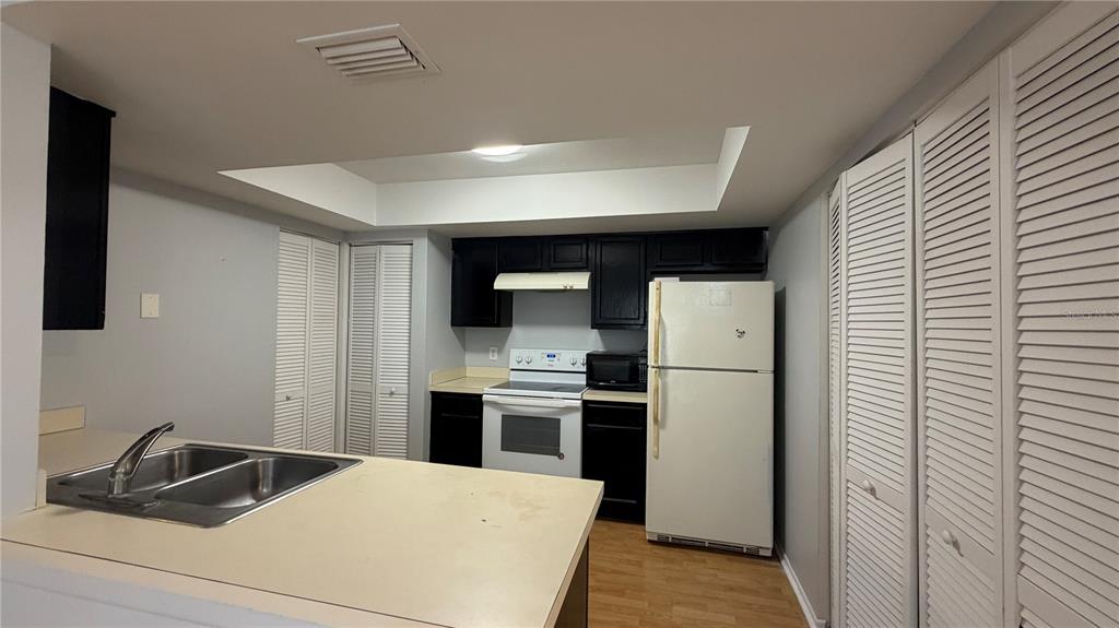 A kitchen features black cabinets, white appliances, a double sink, and louvered closet doors — 4323 PINEBARK AVENUE UNIT 77-1, ORLANDO, FL