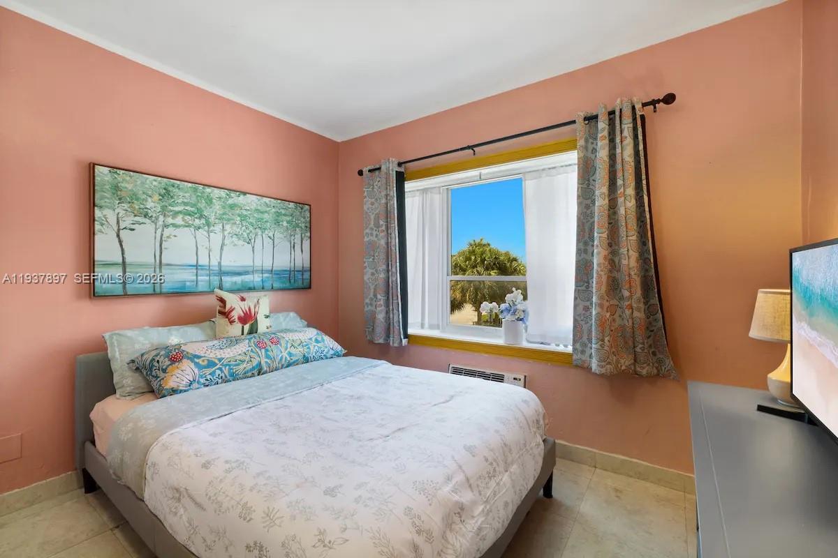 A bedroom with peach walls, a bed, a window with patterned curtains, and tile flooring — 255 W 24th St # 234, Miami Beach FL 33140, MIAMI BEACH, FL