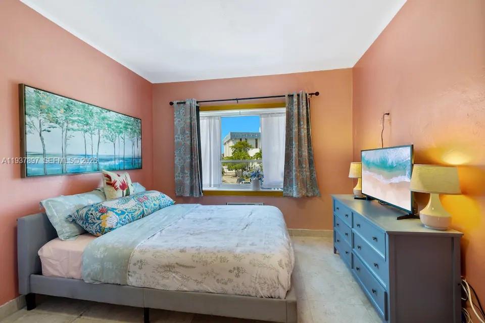A bedroom with peach walls, a grey bed, and a blue dresser under a television — 255 W 24th St # 234, Miami Beach FL 33140, MIAMI BEACH, FL