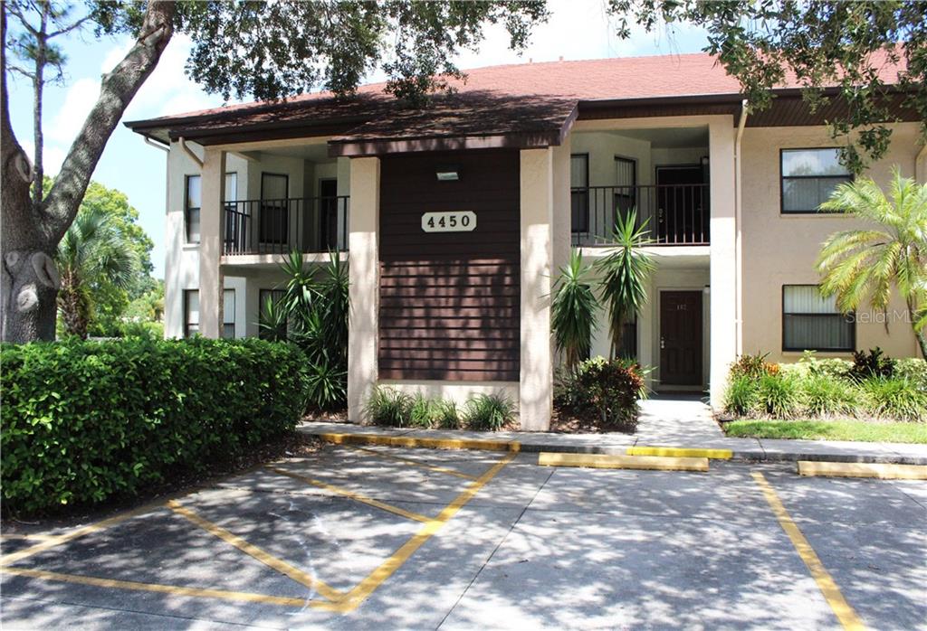 A two-story apartment building exterior features a brown wood-paneled facade, balconies, and a parking lot — 4450 47TH AVENUE W UNIT 102, BRADENTON, FL