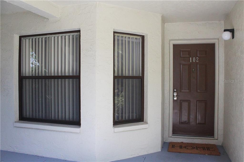 The exterior entrance of a residence features a brown door numbered 102 and two windows — 4450 47TH AVENUE W UNIT 102, BRADENTON, FL