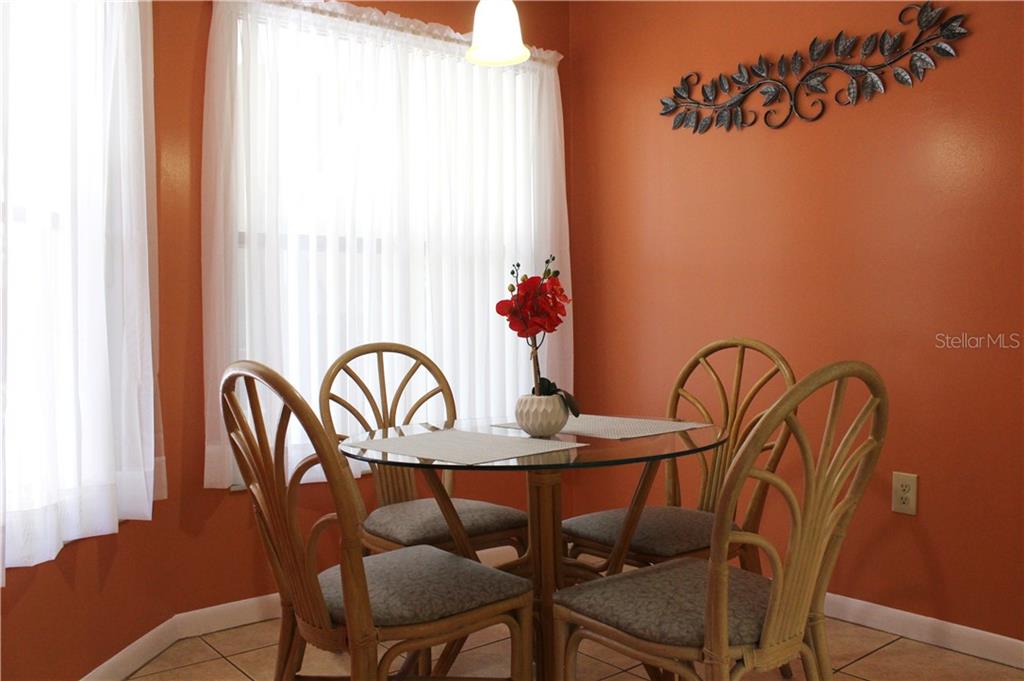 A dining area features a glass-topped table with four rattan chairs against orange walls — 4450 47TH AVENUE W UNIT 102, BRADENTON, FL
