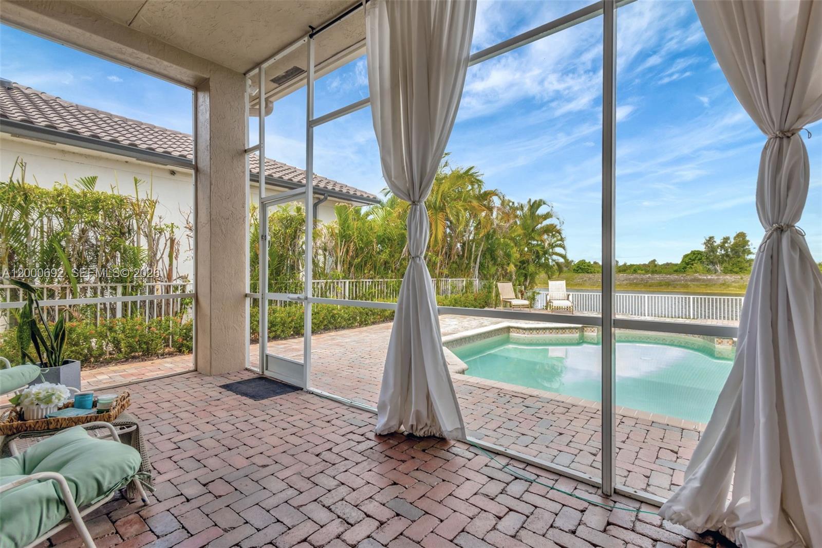 A screened-in brick patio overlooks a swimming pool and a lake with palm trees — 3060 SW 195th Ter, Miramar FL 33029, MIRAMAR, FL