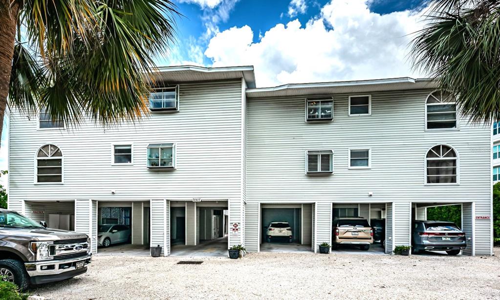 A three-story building with light-colored siding features covered parking bays on the ground level — 20019 GULF BOULEVARD UNIT 9, INDIAN ROCKS BEACH, FL