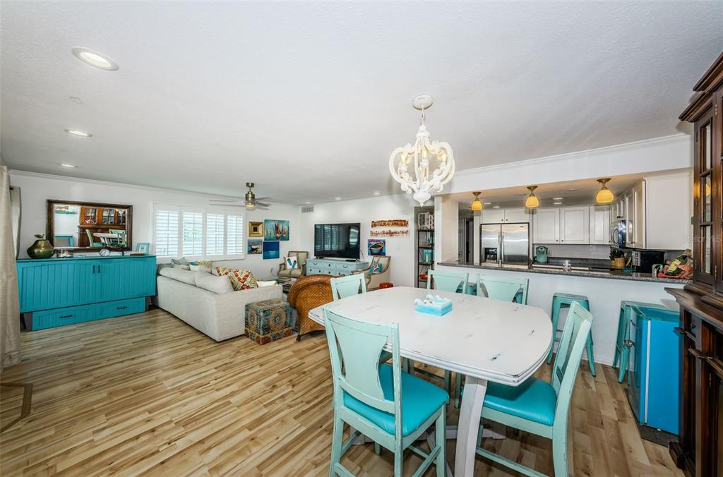 An open-concept living and dining area features light wood floors, turquoise furniture, and a chandelier — 20019 GULF BOULEVARD UNIT 9, INDIAN ROCKS BEACH, FL