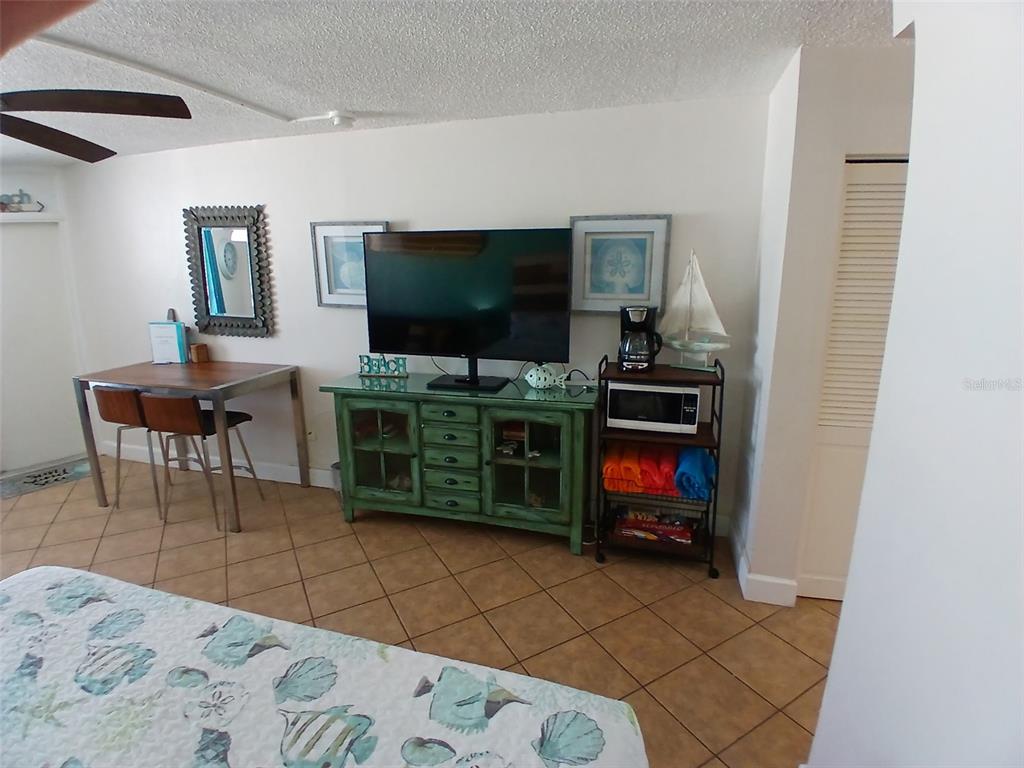 A bedroom features a television on a green cabinet, a small dining table, and tile floors — 313 S ATLANTIC AVENUE UNIT 5160, DAYTONA BEACH, FL