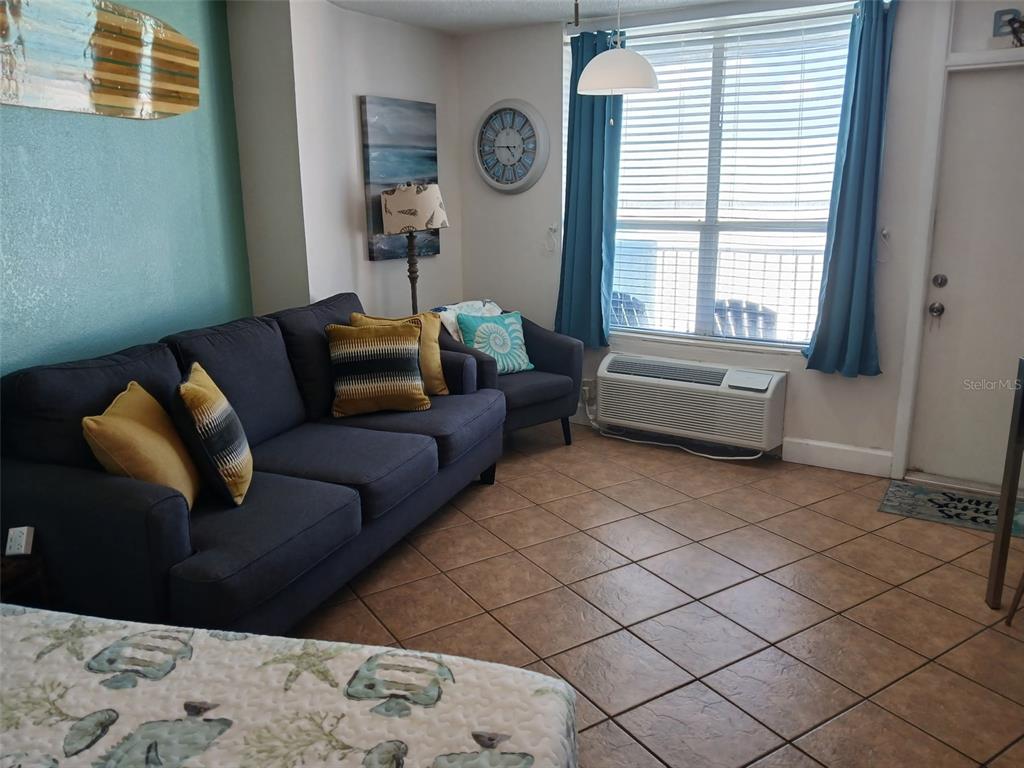 A living room features a dark sofa, tiled floors, a window with blue curtains, and decor — 313 S ATLANTIC AVENUE UNIT 5160, DAYTONA BEACH, FL