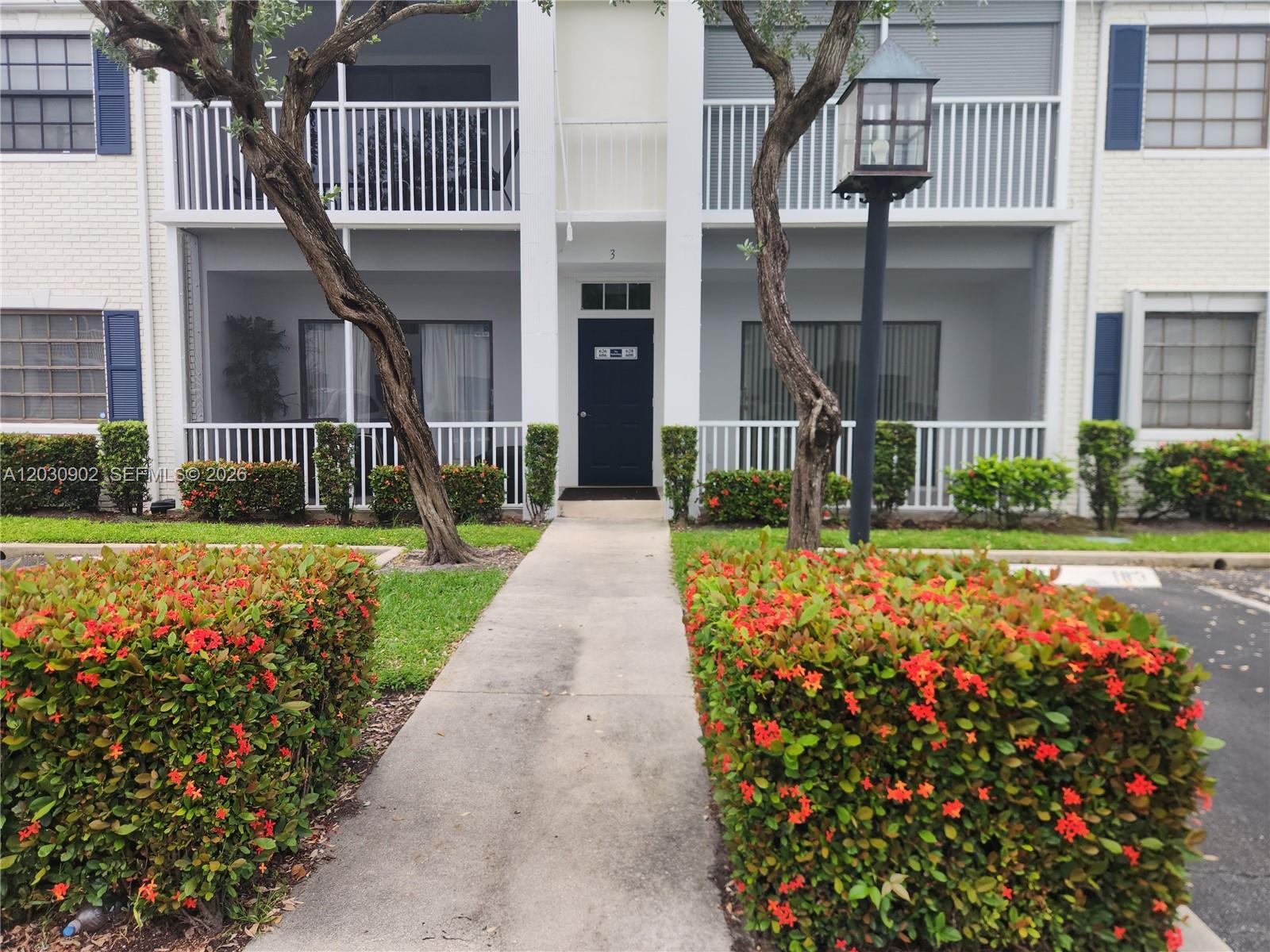 A concrete walkway leads to the entrance of a two-story building with screened balconies — 160 Cypress Club Dr # 608, Pompano Beach FL 33060, POMPANO BEACH, FL