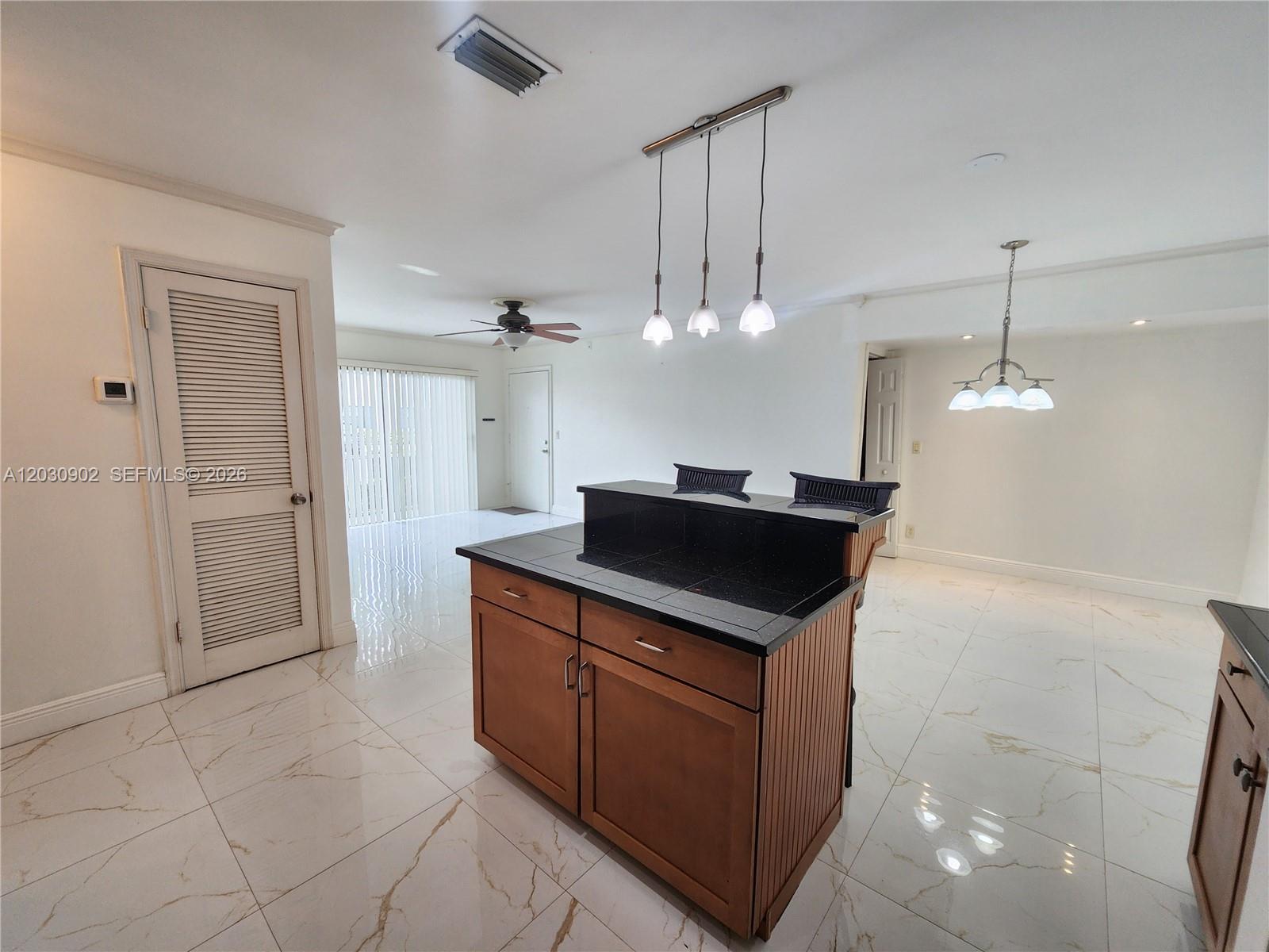 A kitchen island with a black countertop sits in a room with white tile floors — 160 Cypress Club Dr # 608, Pompano Beach FL 33060, POMPANO BEACH, FL