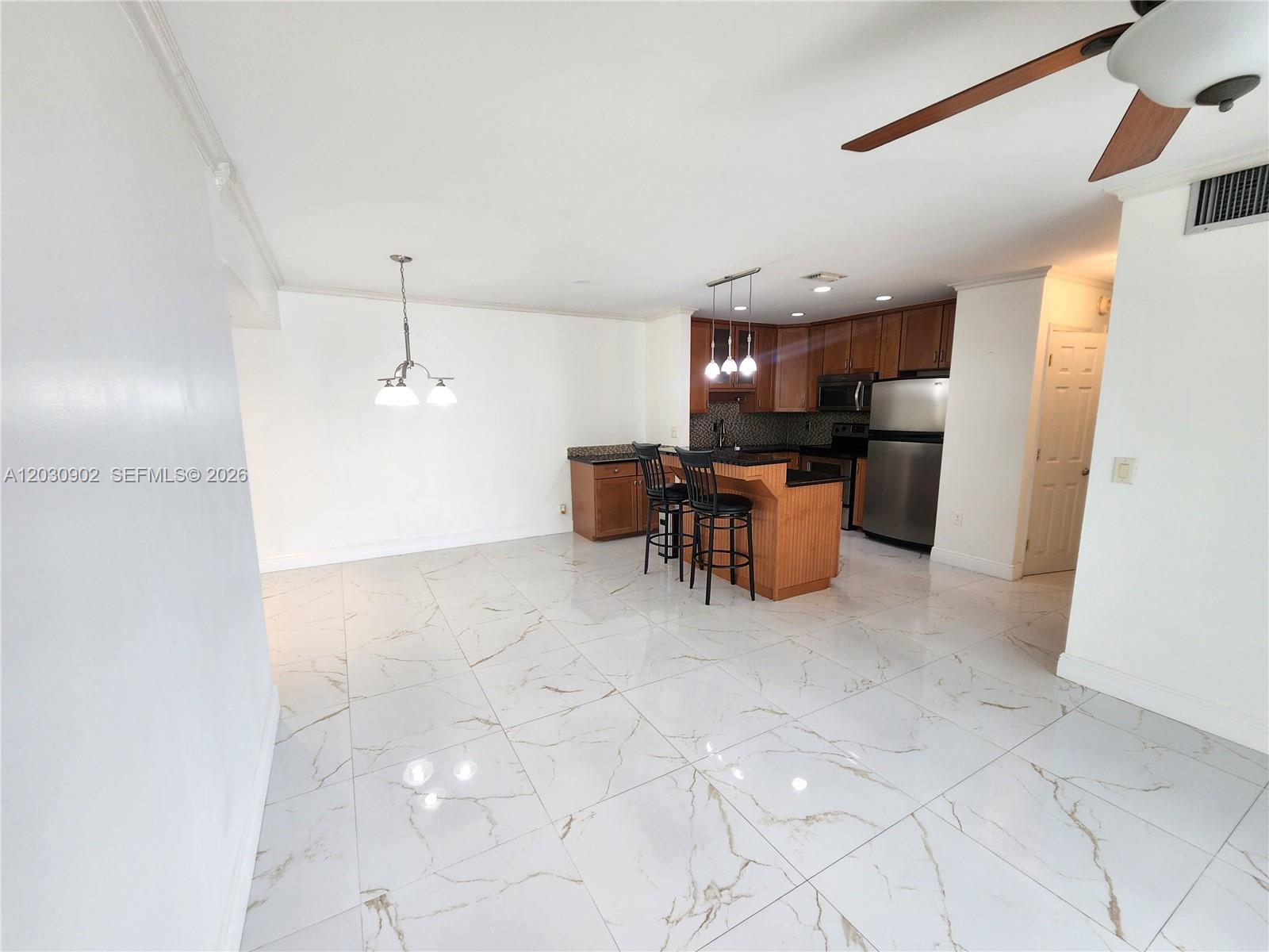 An open-concept kitchen features wood cabinets, stainless steel appliances, and white marble-look tile flooring — 160 Cypress Club Dr # 608, Pompano Beach FL 33060, POMPANO BEACH, FL