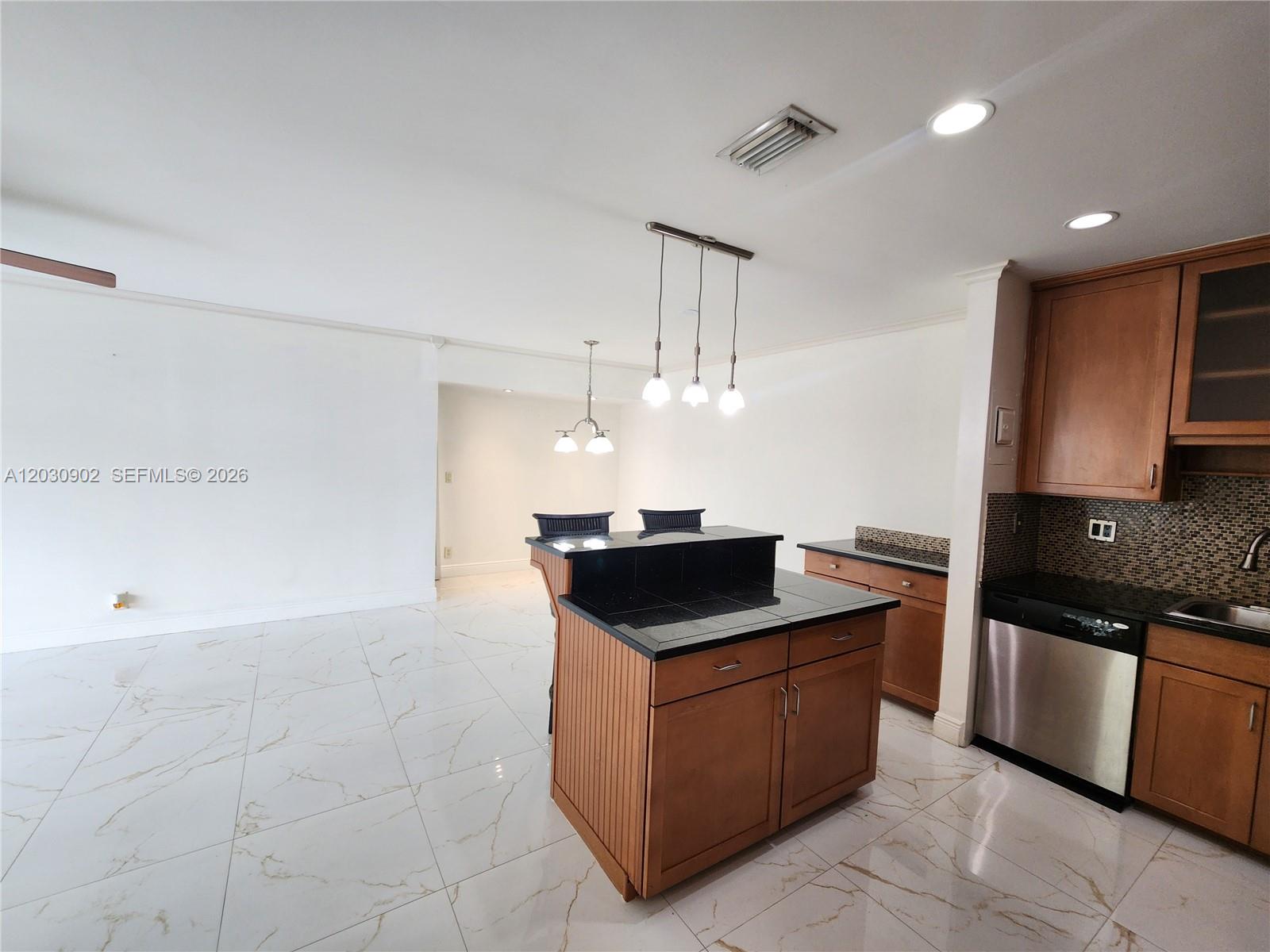 A kitchen features a black-topped island, wooden cabinets, and white marble-patterned tile flooring — 160 Cypress Club Dr # 608, Pompano Beach FL 33060, POMPANO BEACH, FL