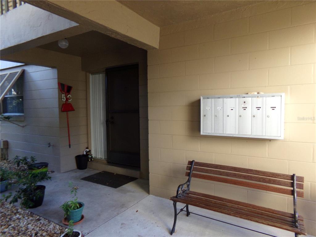 An exterior view of a building entrance with a wooden bench and wall-mounted mailboxes — 110 CYPRESS WOODS CT UNIT 5C, DELTONA, FL