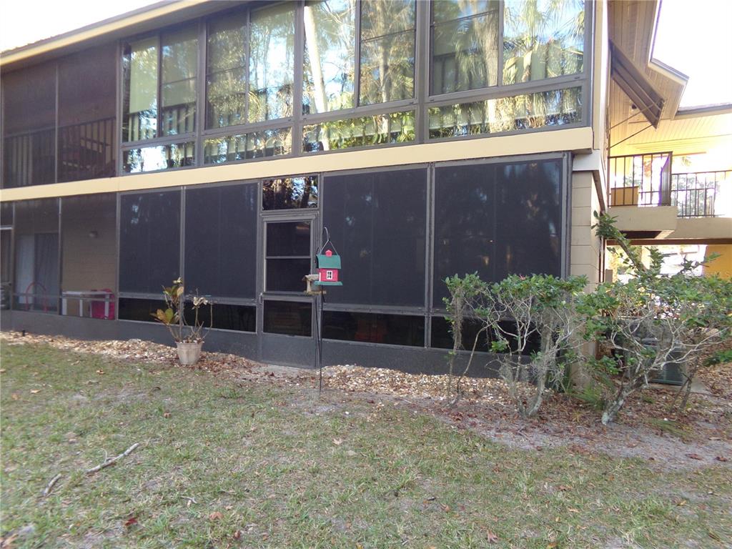 A two-story building features a screened-in ground floor patio and large windows above — 110 CYPRESS WOODS CT UNIT 5C, DELTONA, FL