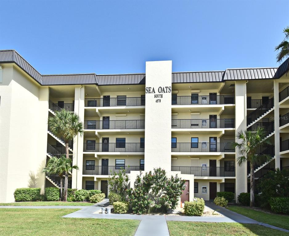 A multi-story apartment building with balconies and palm trees under a clear blue sky — 4570 OCEAN BEACH BOULEVARD UNIT 42, COCOA BEACH, FL