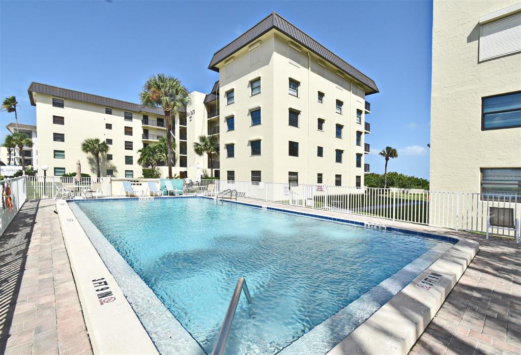 A rectangular swimming pool sits in front of a multi-story apartment building with palm trees — 4570 OCEAN BEACH BOULEVARD UNIT 42, COCOA BEACH, FL