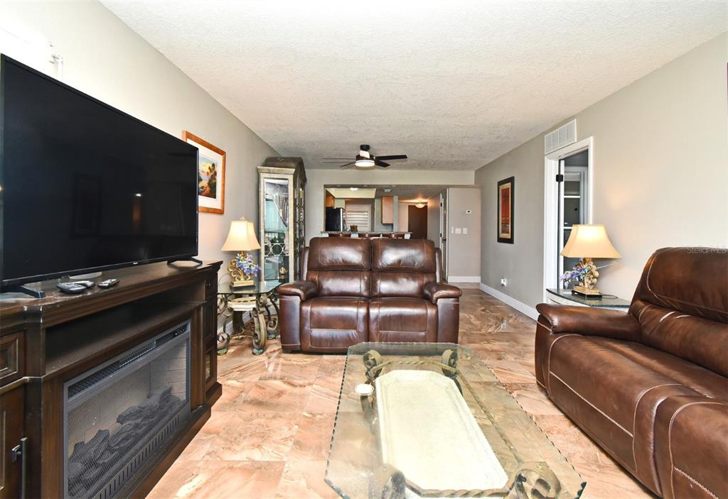 A living room features brown leather sofas, a glass coffee table, and marble-look tile flooring — 4570 OCEAN BEACH BOULEVARD UNIT 42, COCOA BEACH, FL