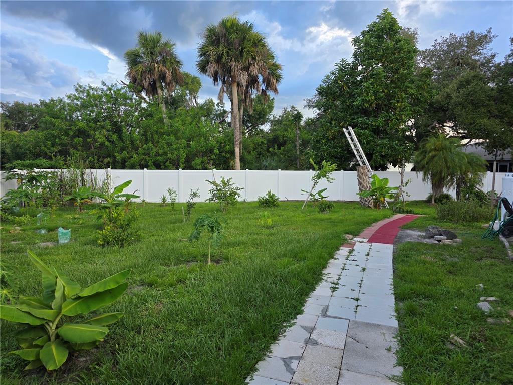 A grassy backyard features a stone walkway, young fruit trees, and a white privacy fence — 4943 BECKHAM COURT, NORTH PORT, FL