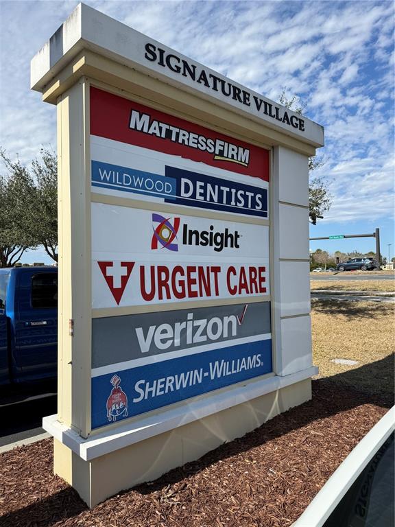 A tall, multi-tenant commercial sign for Signature Village stands outdoors on a sunny day — 4675 E SR 44 DRIVE UNIT 106, WILDWOOD, FL