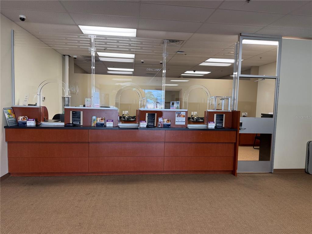 A bank teller counter with glass partitions and wood cabinetry in a carpeted room — 4675 E SR 44 DRIVE UNIT 106, WILDWOOD, FL