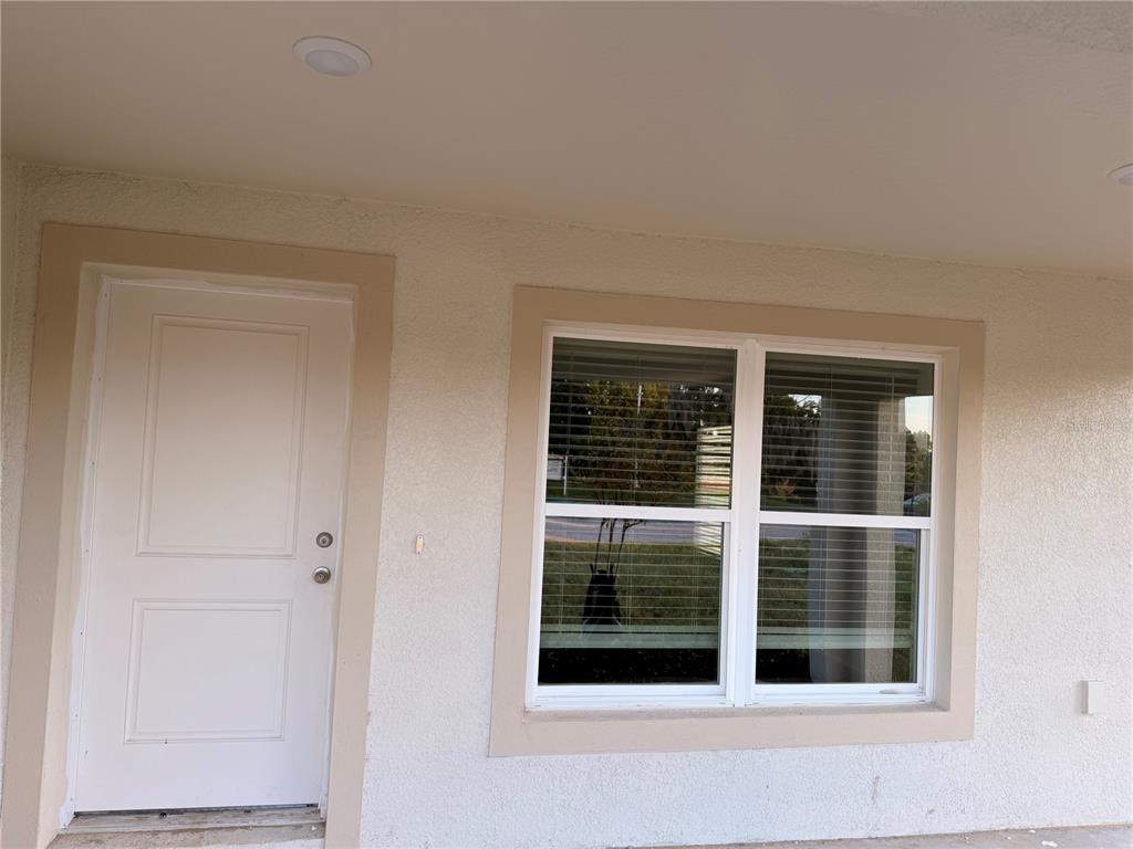 A white door and a large window with blinds are set into a stucco exterior wall — 445 ALVINA AVENUE, LAKE WALES, FL