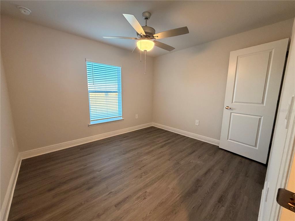 An empty bedroom features wood-look flooring, a ceiling fan, a window with blinds, and a door — 445 ALVINA AVENUE, LAKE WALES, FL