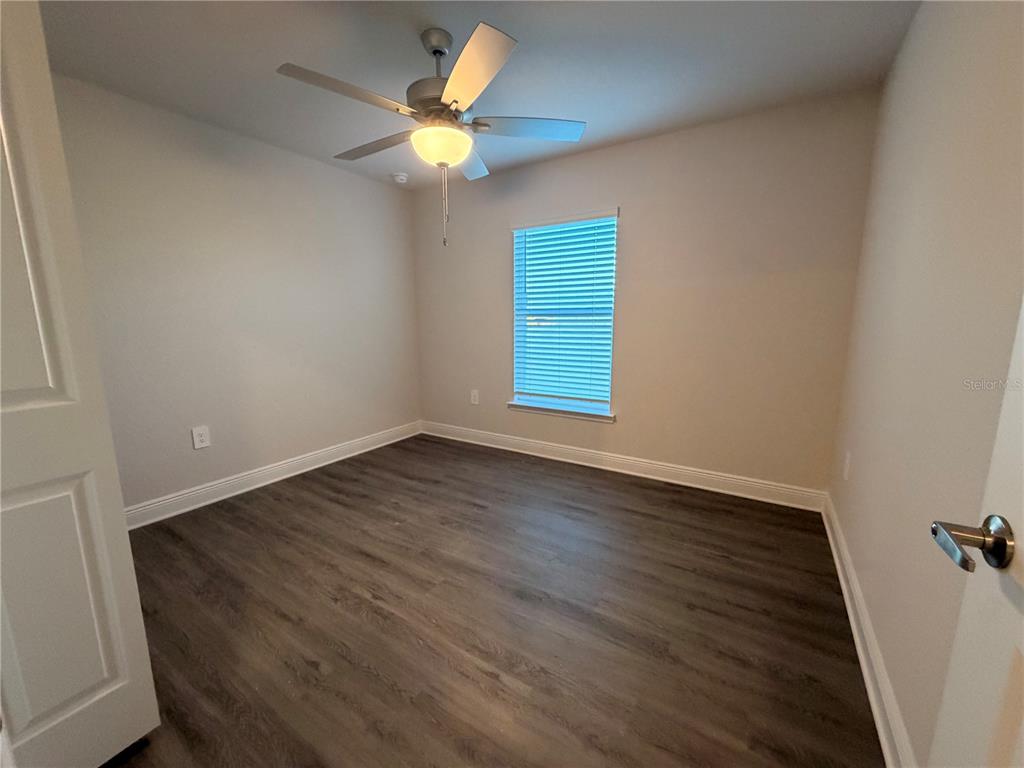 An empty bedroom features light gray walls, dark wood-look flooring, a ceiling fan, and a window — 445 ALVINA AVENUE, LAKE WALES, FL
